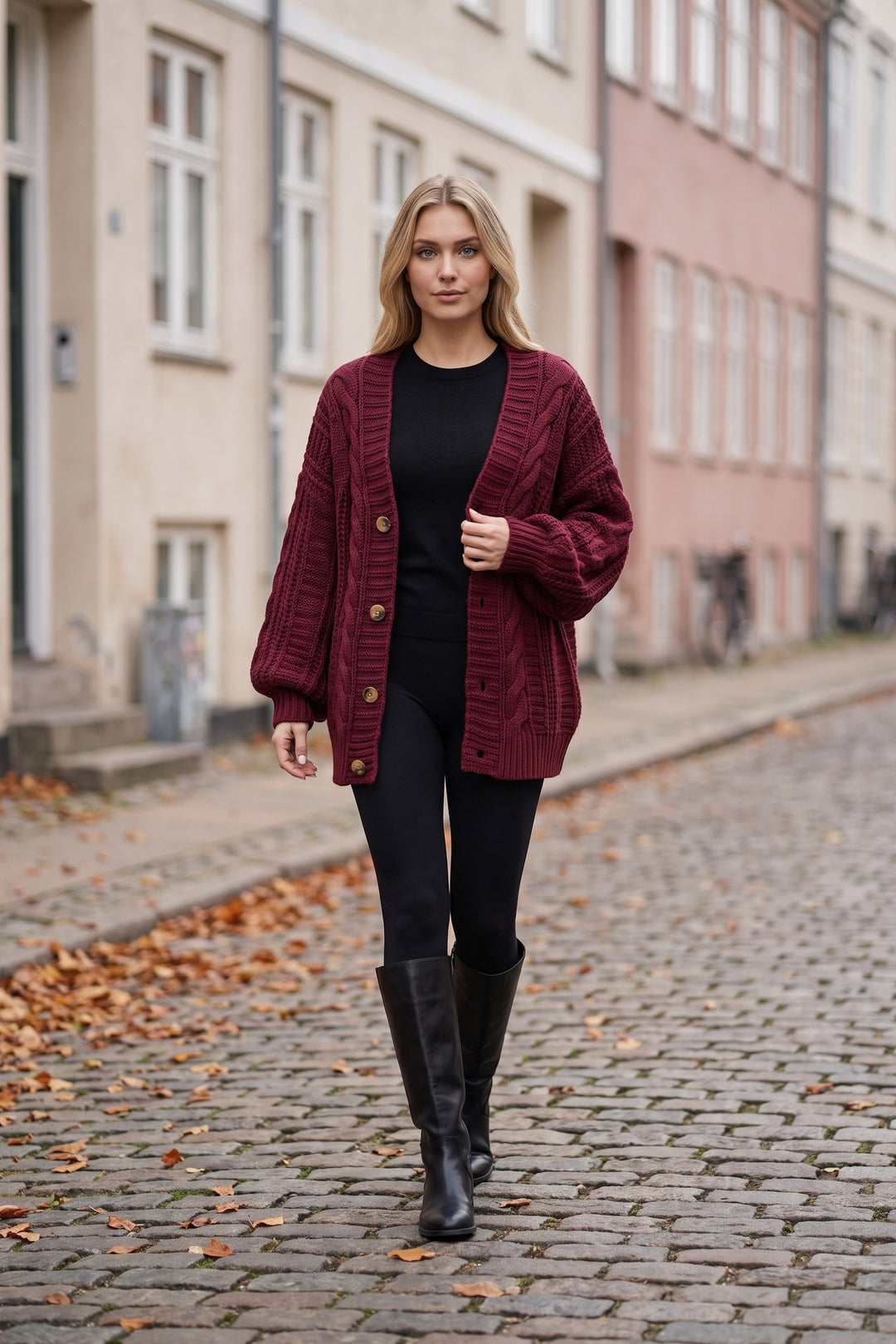 Kvinde i bordeauxrød oversized kabelstrikket cardigan med træknapper på en brostensbelagt gade om efteråret