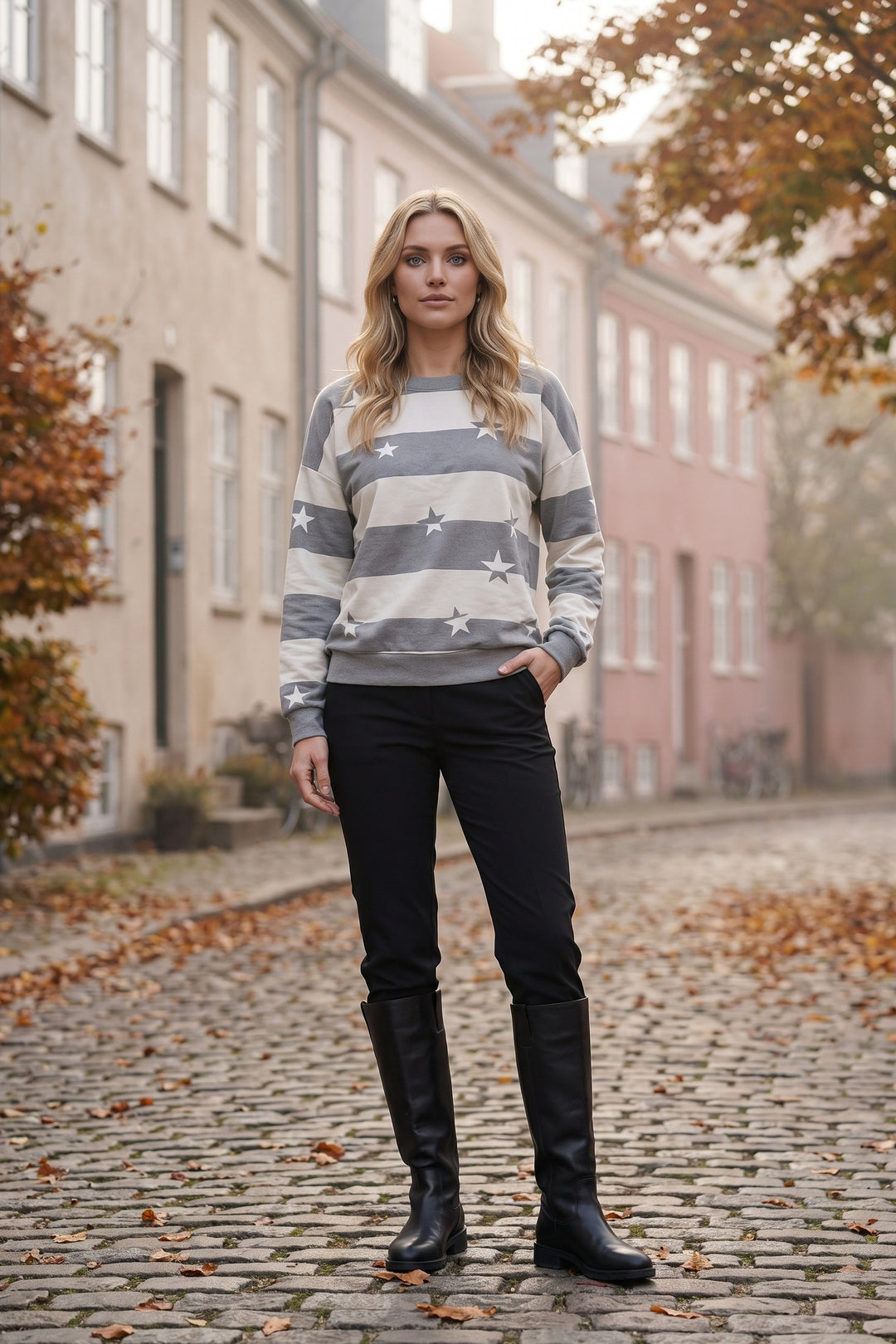 Kvinde i grå og offwhite stribet sweatshirt med hvidt stjerneprint på en brostensbelagt gade om efteråret